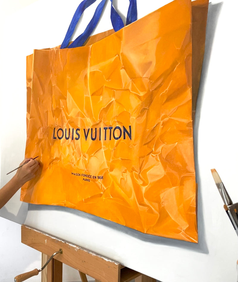 Cecilia Mendoza painting an orange Louis Vuitton shopping bag on an easel with a brush in her study in Italy