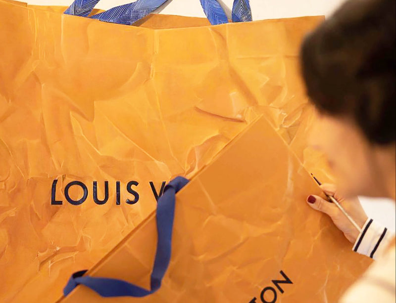 Cecilia Mendoza, CM Visual artist, is painting a Large orange Louis Vuitton shopping bag with blue handles in her studio in Itay.