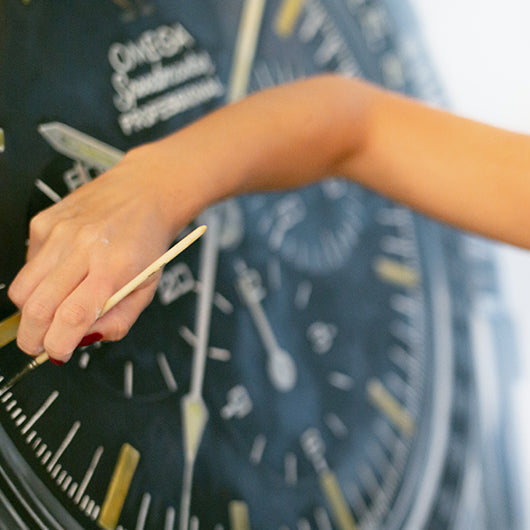 Cecilia Mendoza, known as CM Visual Artist, painting an Omega Speedmaster-inspired watch artwork.
